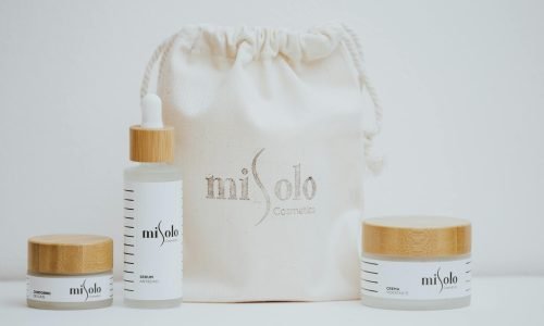 Minimalist photo of organic skincare products with bamboo lids and a canvas bag on a white background.